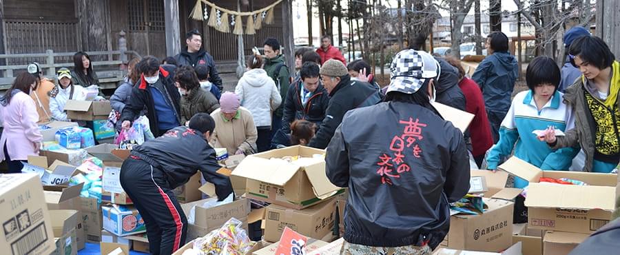 神社の前で支援物資の入った大量の段ボール箱を開ける被災地の人々