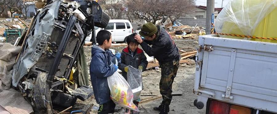 車が横倒しになった被災地でゴミを拾う子供たちと加藤代表
