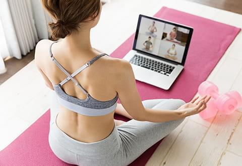 ピンク色のヨガマットの上にノートパソコンを置き、瞑想を行う女性