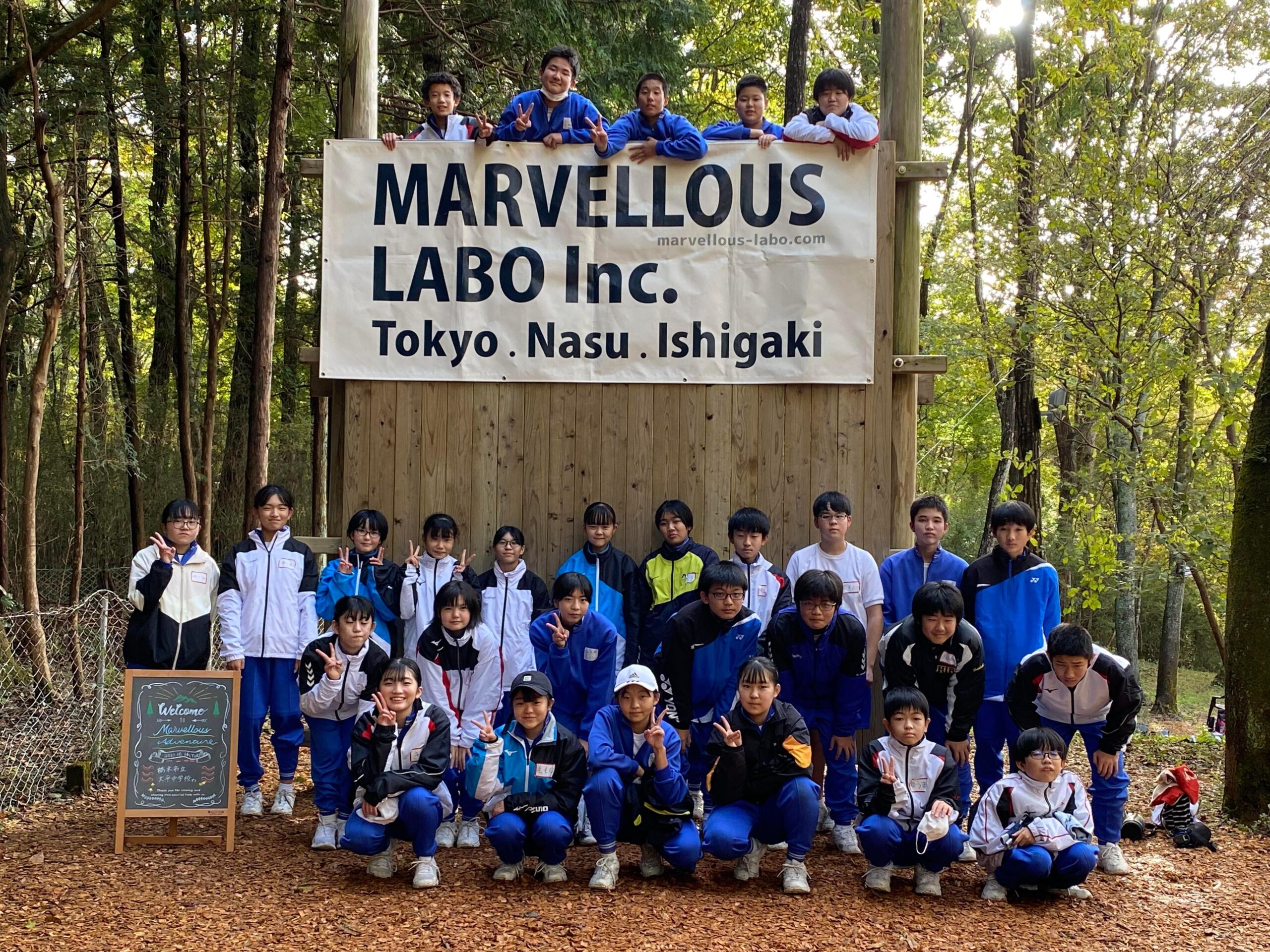 「MARVELLOUS LABO」の旗を取り付けた木製の壁の前に整列する参加者たち（栃木市立大平中学校03）